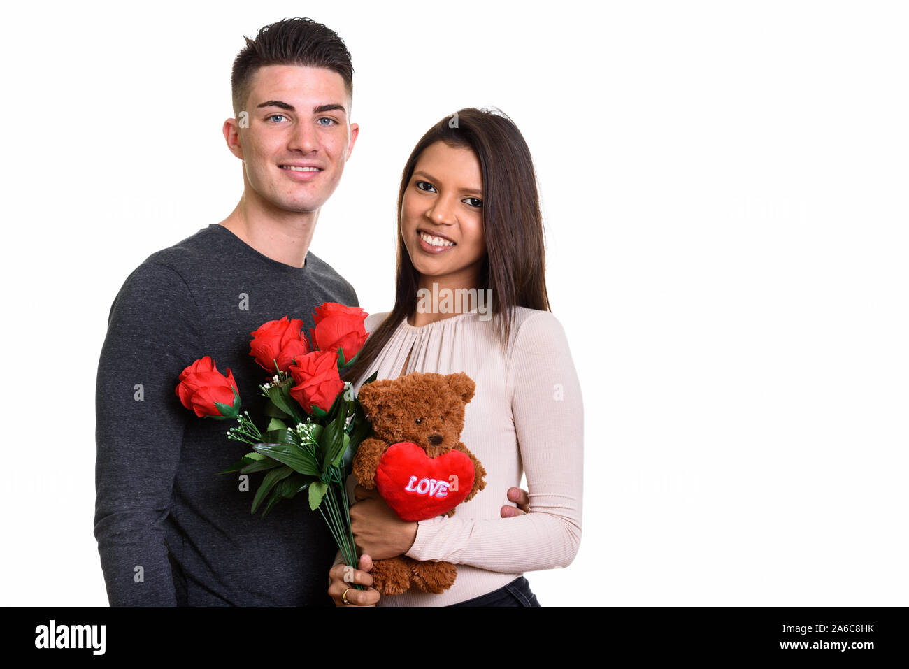 Young happy couple smiling while holding roses rouges et teddy bea Banque D'Images