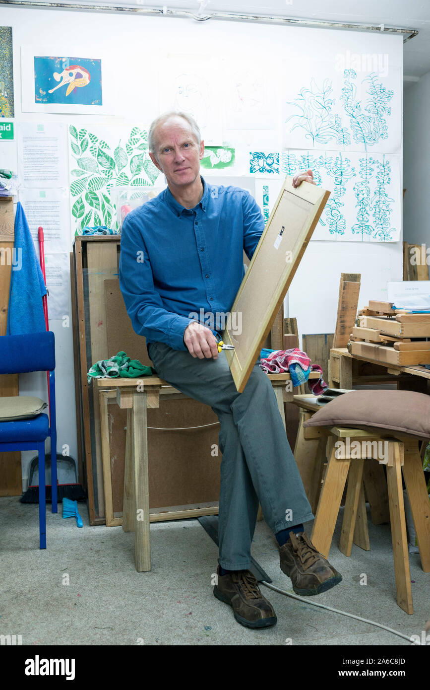 Un framer d'images masculin est assis dans son atelier, tenant un cadre. Banque D'Images