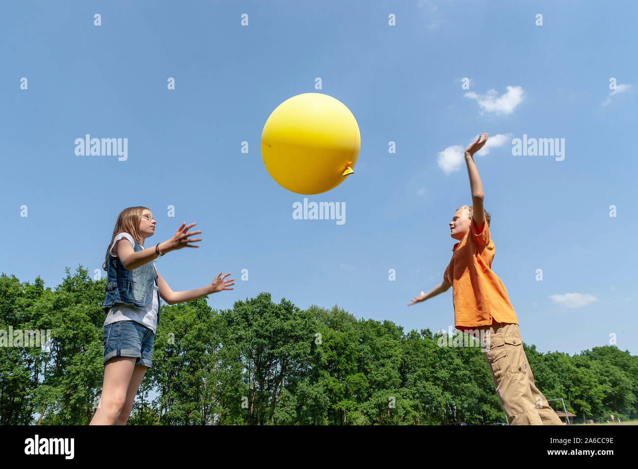 Un garçon et une fille sont en train de jouer avec un gros ballon jaune. Banque D'Images