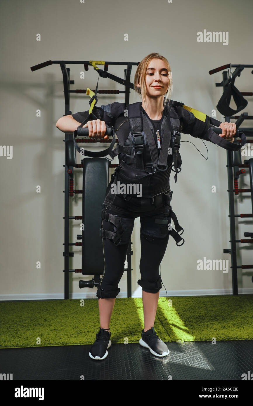 Très jolie jeune femme portant dans les détecteurs et ceintures, se fixe avec du velcro pratique EMS fitness dans l'exécution d'exercices de gymnastique de traction. Im électrique Banque D'Images