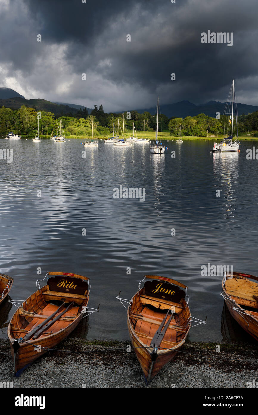 Voiliers amarrés sur le lac Windermere avec barques sur le rivage à Waterhead Ambleside dans soleil du matin avec des nuages sombres Lake District National Park Banque D'Images