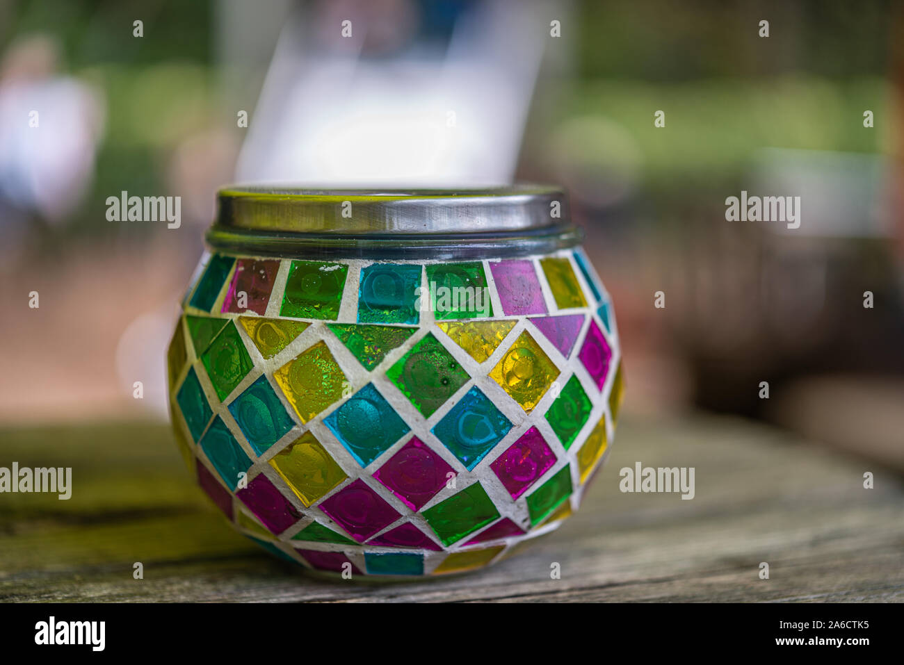 Bougie en verre multicolore stand avec un couvercle de métal sur une table en bois contre un arrière-plan flou Banque D'Images