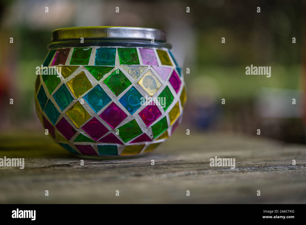 Bougie en verre multicolore stand avec un couvercle de métal sur une table en bois contre un arrière-plan flou Banque D'Images