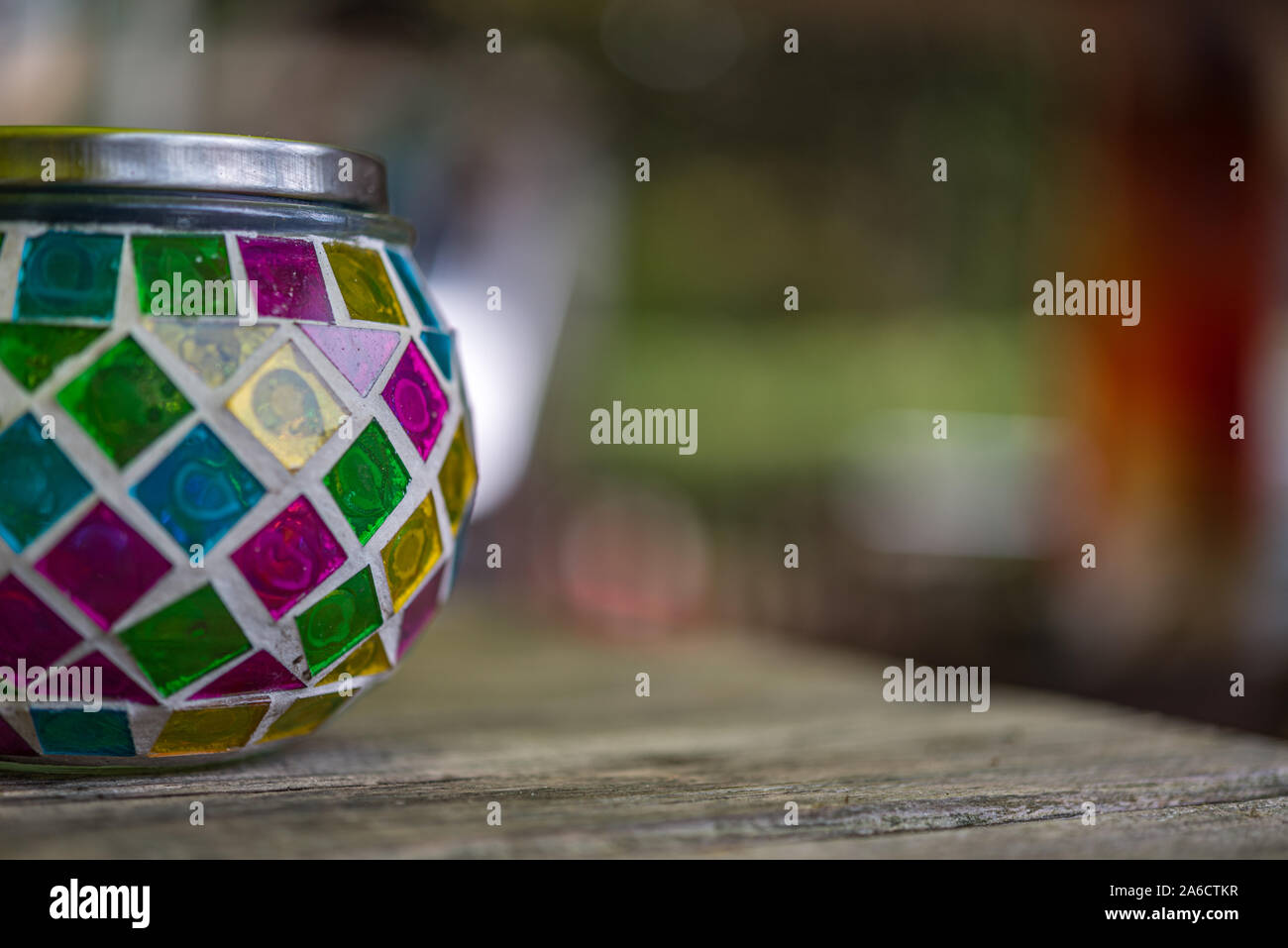 Bougie en verre multicolore stand avec un couvercle de métal sur une table en bois contre un arrière-plan flou Banque D'Images