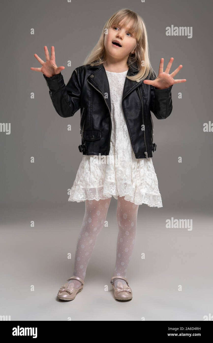 Petite blonde jeune fille en robe blanche et veste en cuir noire pose  debout sur un fond gris Photo Stock - Alamy