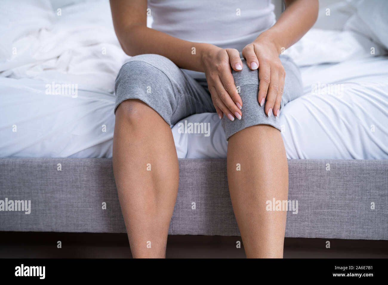 Femme souffrant de douleur au genou assis au lit Banque D'Images