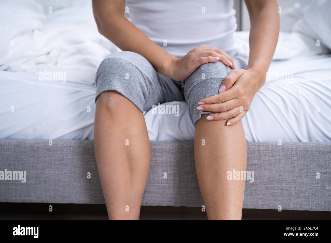 Femme souffrant de douleur au genou assis au lit Banque D'Images