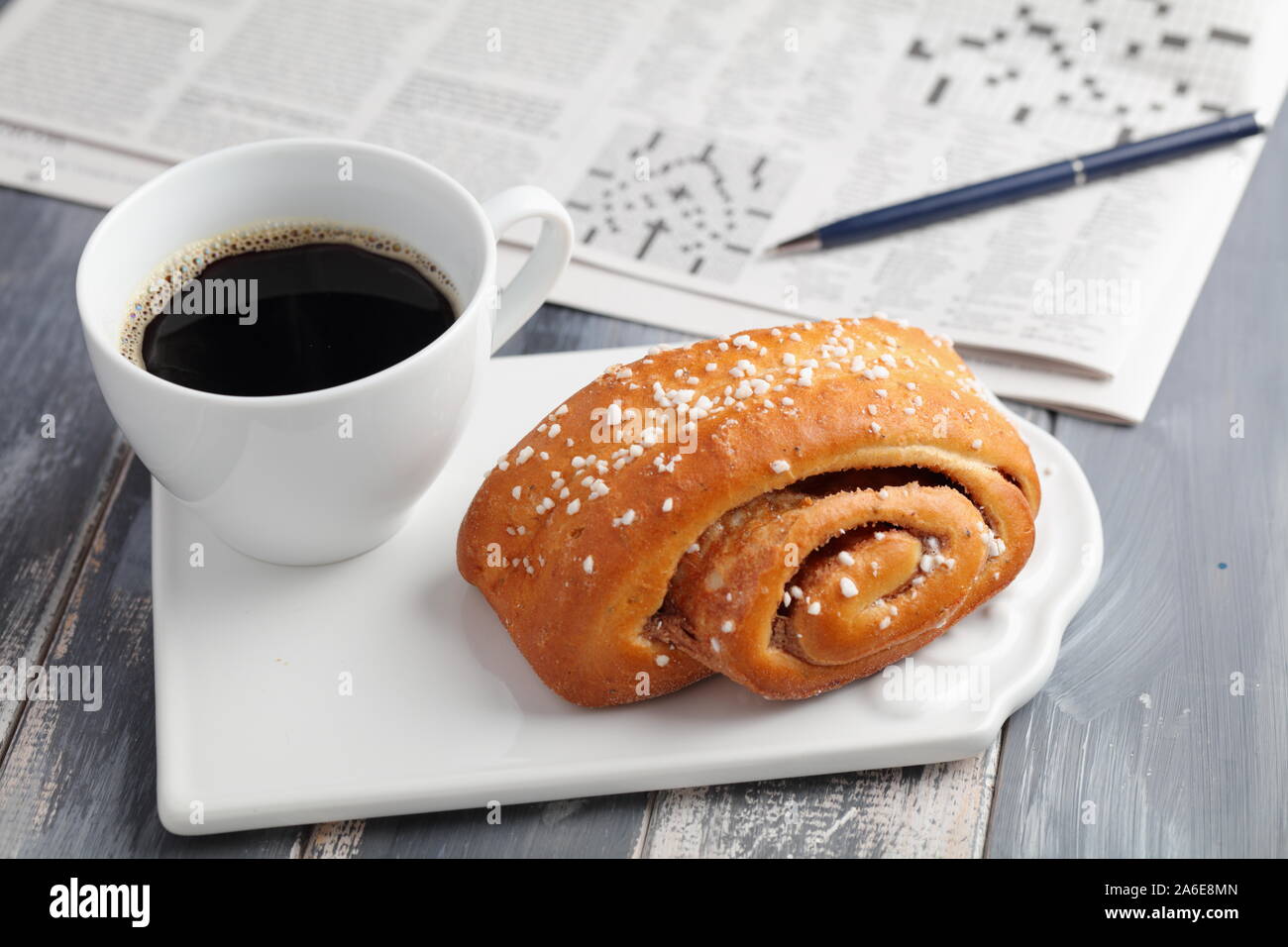 Gâteau suédois à la cannelle et une tasse de café noir contre un journal avec mots croisés Banque D'Images