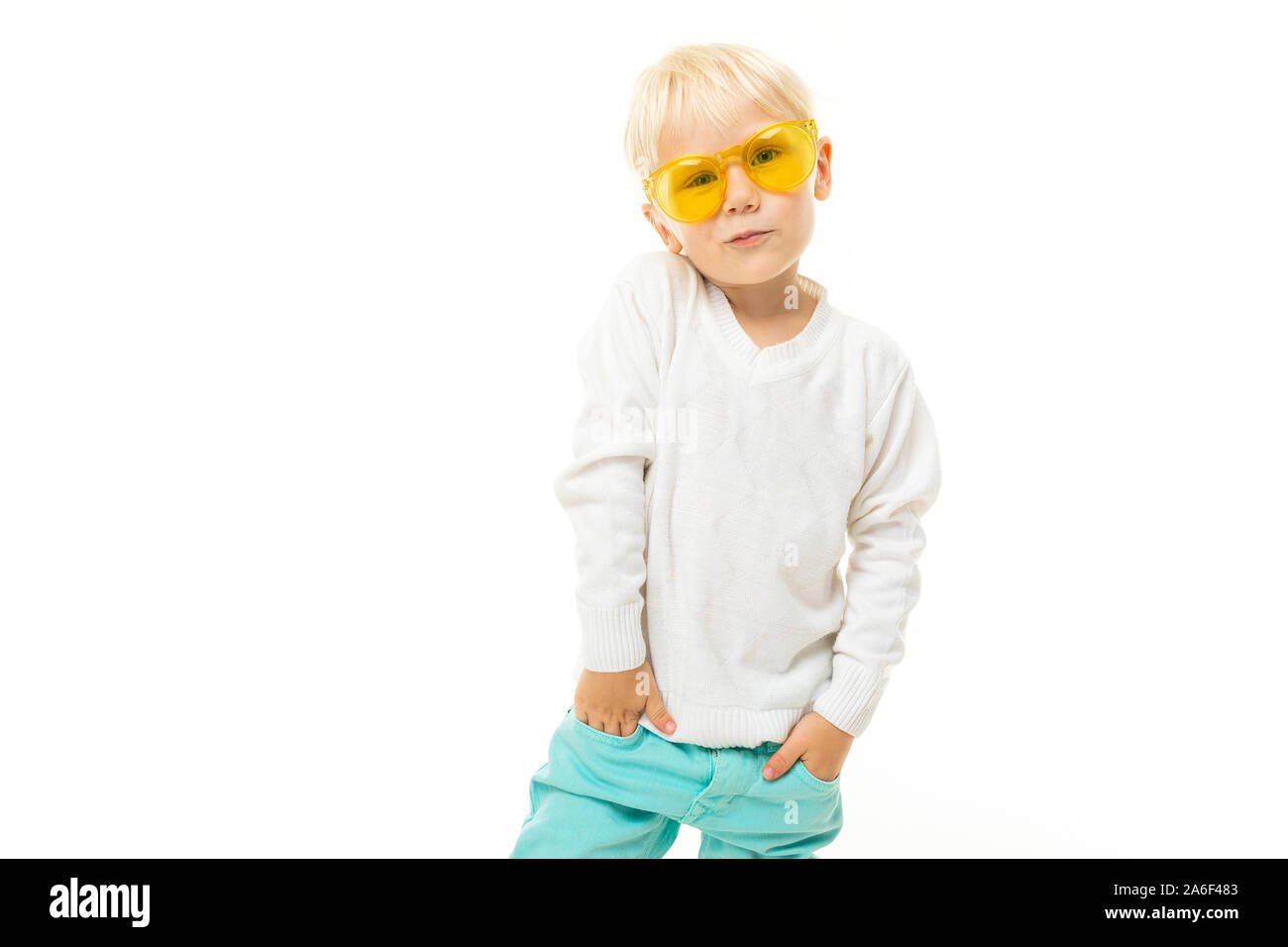 Petit garçon aux cheveux blonds courts, yeux bleus, apparence mignonne, en veste blanche, un pantalon bleu clair, se dresse avec verres jaunes et pose magnifiquement sur Banque D'Images