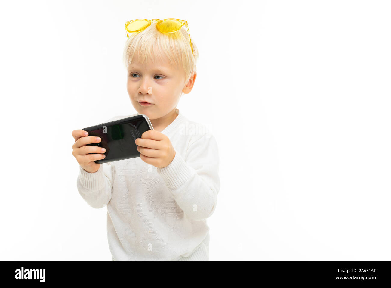 Petit garçon aux cheveux blonds courts, yeux bleus, apparence mignonne, en veste blanche, un pantalon bleu clair, se dresse avec verres jaunes et attend dans le téléphone Banque D'Images