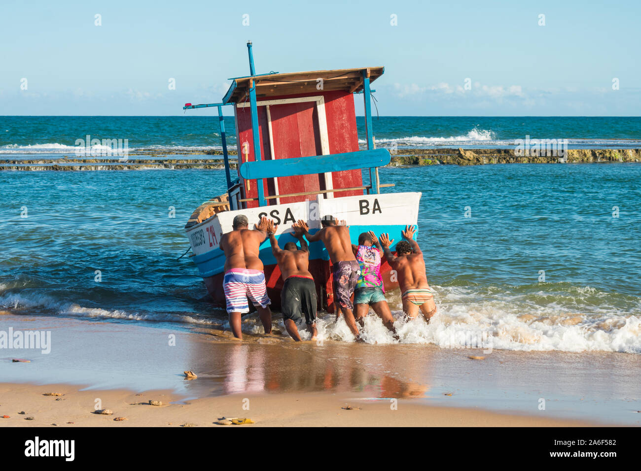 Cinq hommes poussant un bateau de pêche dans l'océan à Arembepe, Bahia - Brésil Banque D'Images