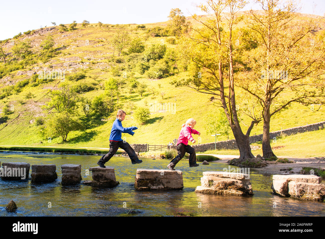 Un petit garçon et fille dans l'espoir, sautant par dessus le Dovedale stepping stones à travers une rivière, ruisseau dans le parc national de Peak District, Derbyshire, l'Autisme Banque D'Images