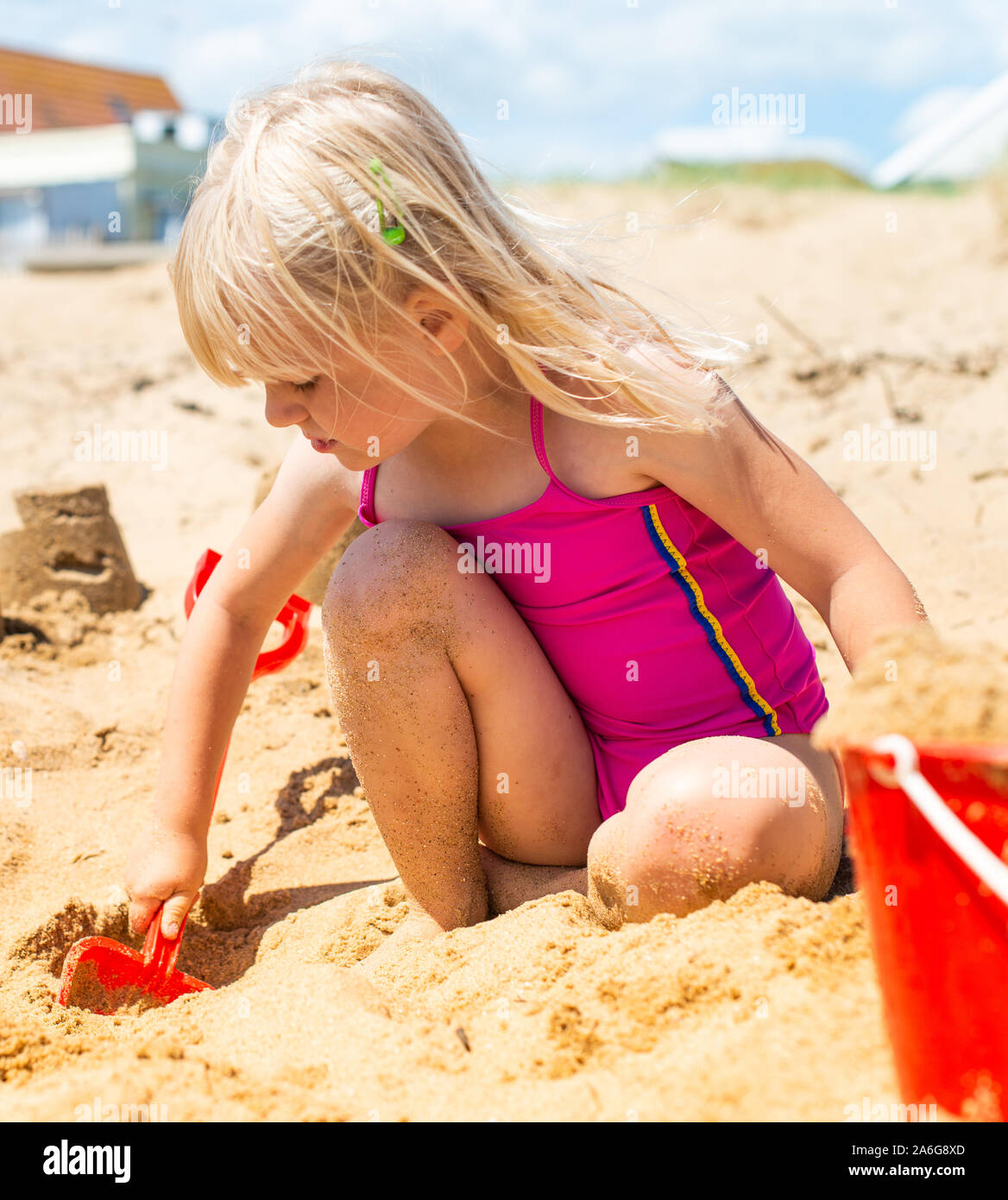 Un mignon, jolie petite fille de creuser et faire des châteaux de sable  avec un seau rouge et la cosse sur la plage par la mer Photo Stock - Alamy