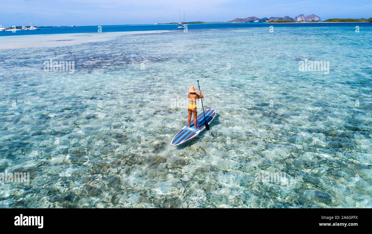 Drone aérien bird's eye view photo de jeune femme pratiquant ou sup paddle board in tropical Caribbean sapphire crystal clear eaux calmes Banque D'Images