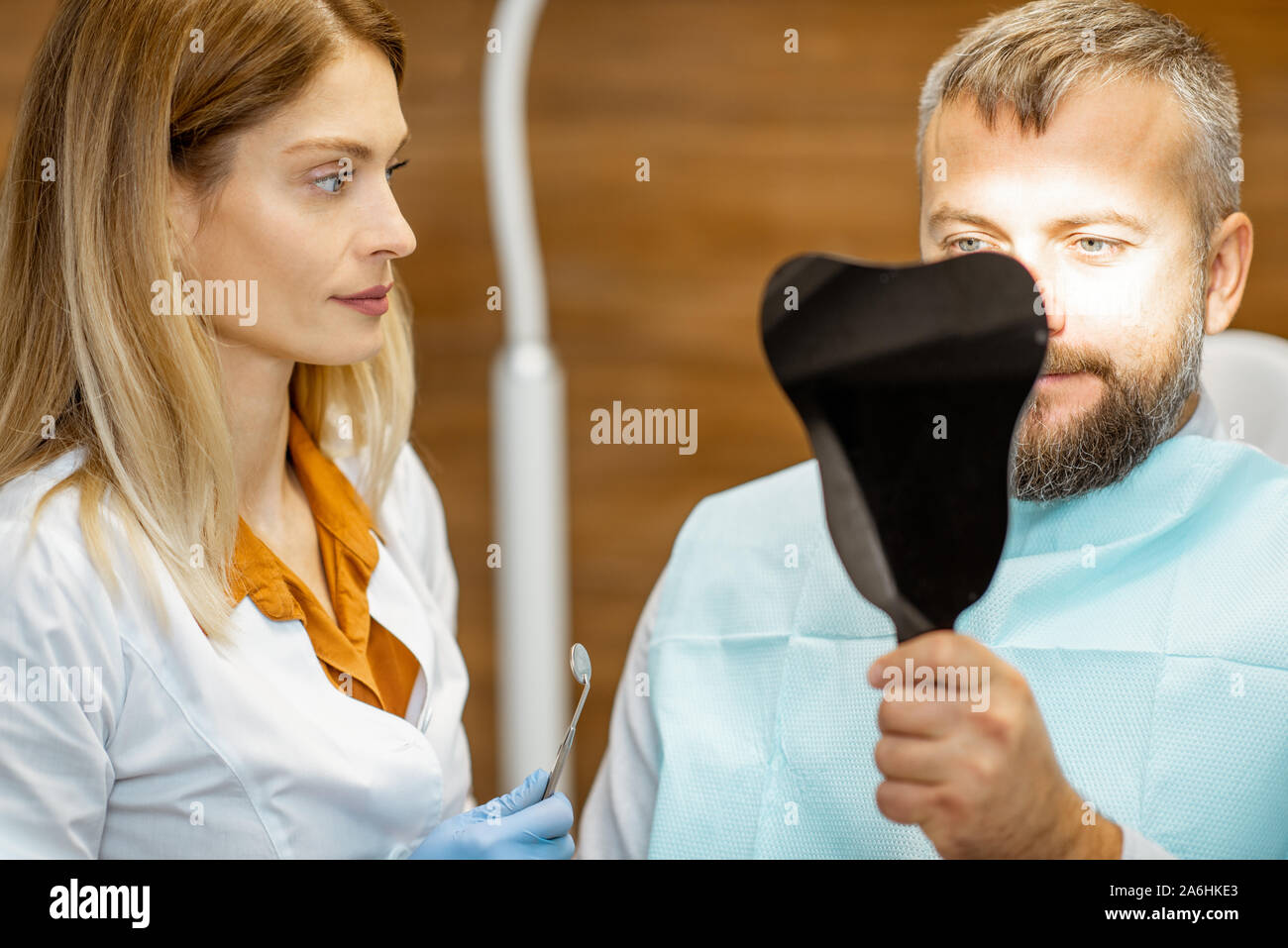 L'homme à la recherche sur le miroir dentaire, satisfait de ses dents, lors d'une consultation médicale avec femme dentiste au cabinet dentaire Banque D'Images