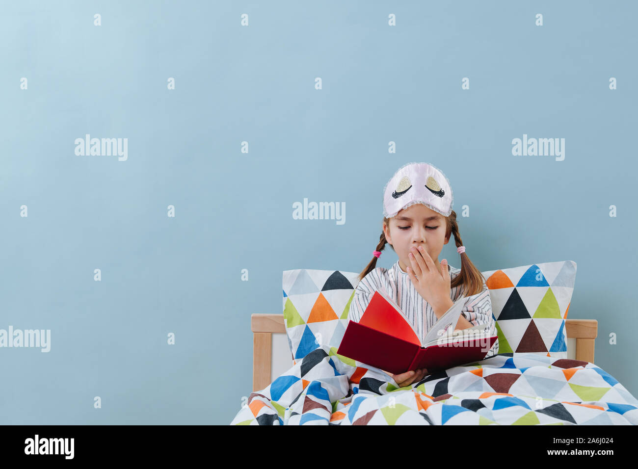 Le bâillement petite fille est en train de lire au lit en pyjama avant d'aller dormir sur blue Banque D'Images