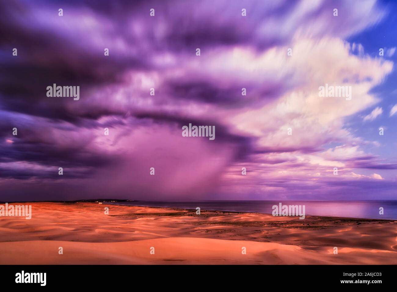 Ciel avec nuages haut floue au coucher du soleil reflétant la lumière sur la dernière journée de l'océan Pacifique et des dunes de sable de Stockton Beach en Australie - paysage marin coloré Banque D'Images