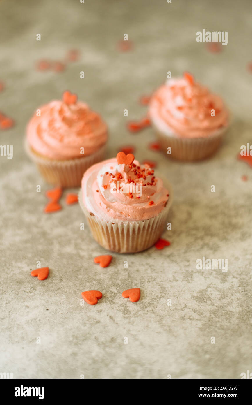 Cupcakes rose sur fond gris pour la Saint-Valentin. Bonbons cadeaux avec de la crème et saupoudrer avec le coeur. Banque D'Images