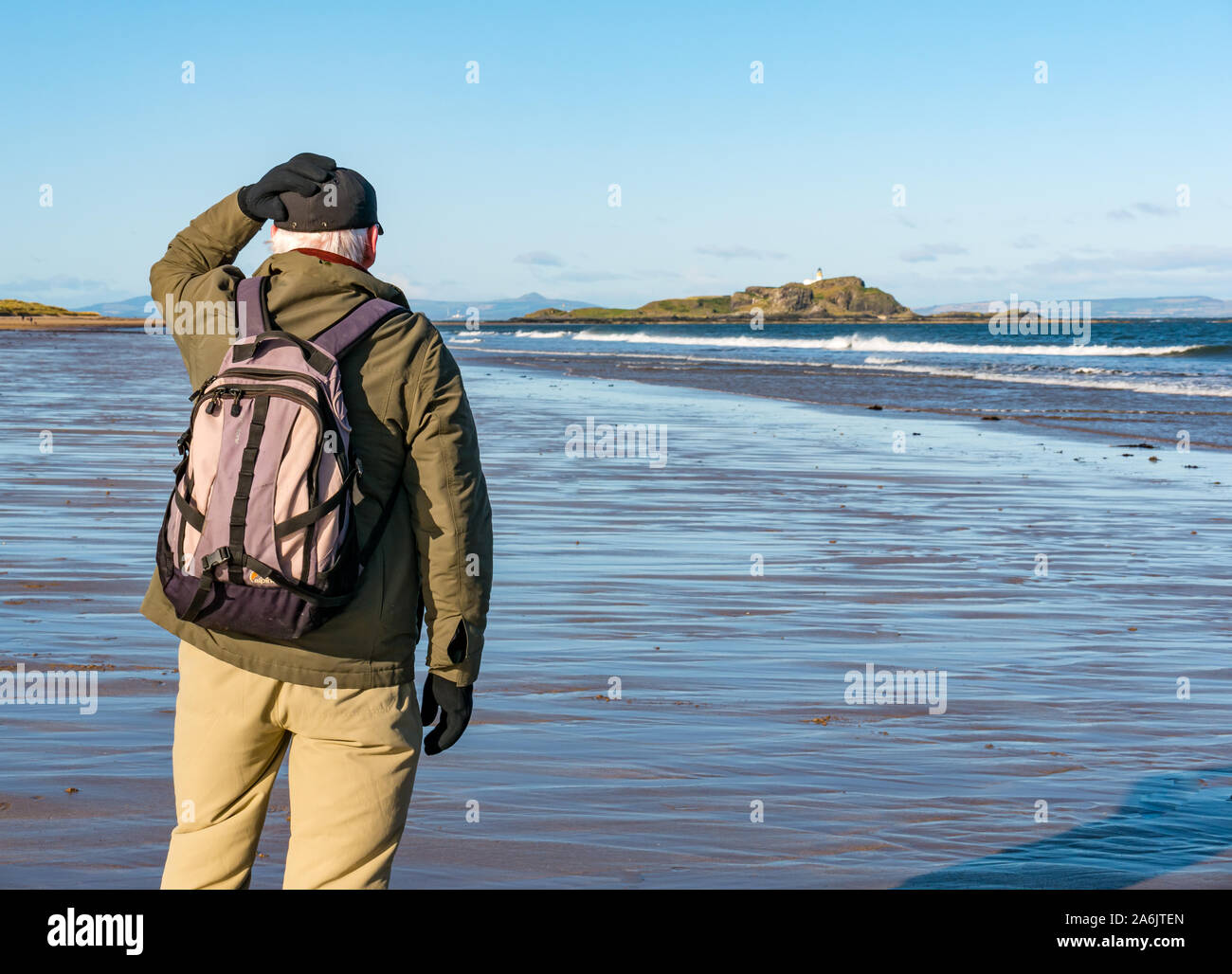 Firth of Forth, East Lothian, UK. 27 octobre 2019. Météo France : A senior man tient son chapeau lors d'une froide mais ensoleillé jour de vent le long de la côte entre Dirleton et North Berwick avec Fidra Island à l'horizon Banque D'Images