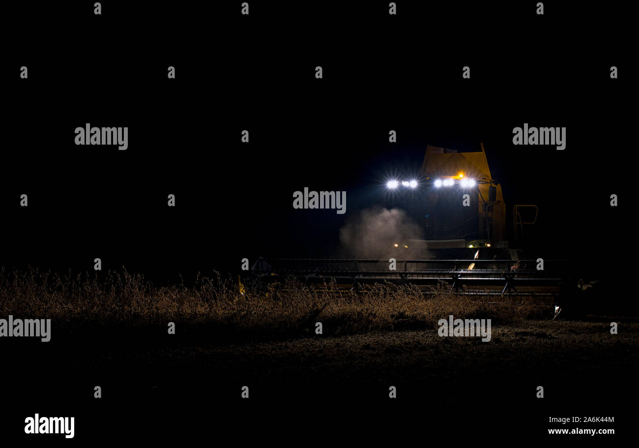 La récolteuse est présent dans le domaine de la soirée. Le blé récolté à nuit Banque D'Images