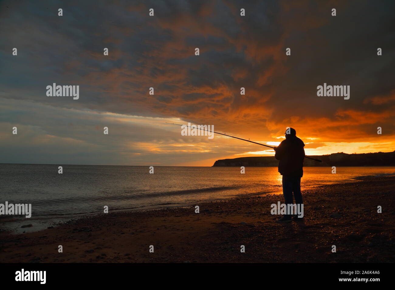 Silhouette de pêcheur sur la côte jurassique au coucher du soleil Banque D'Images