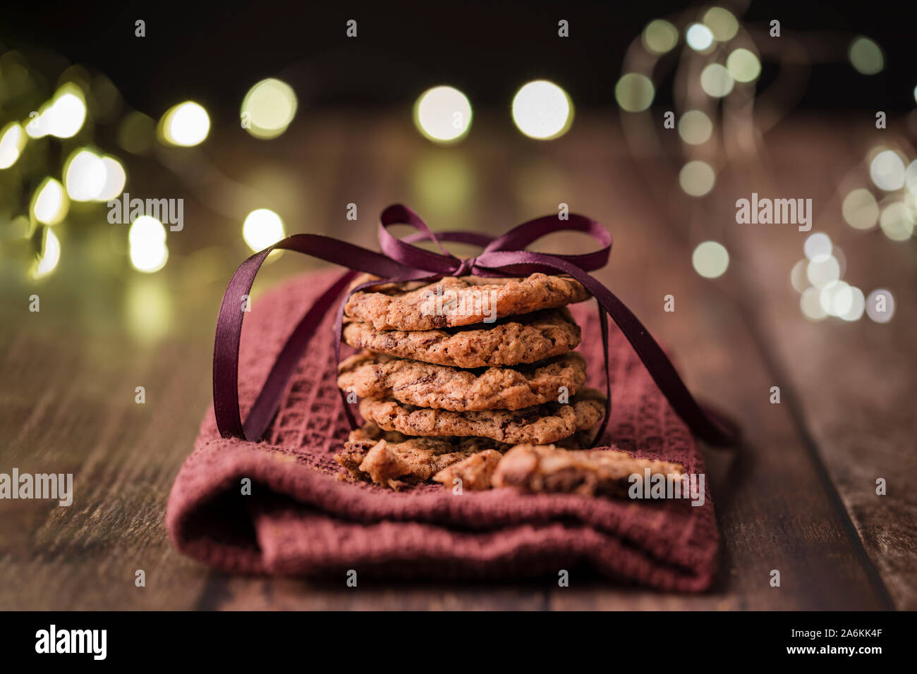 Une pile de délicieux cookies aux pépites de chocolat attaché avec un ruban violet, sur une serviette. Sur une table en bois avec string lumières dans l'arrière-plan Banque D'Images