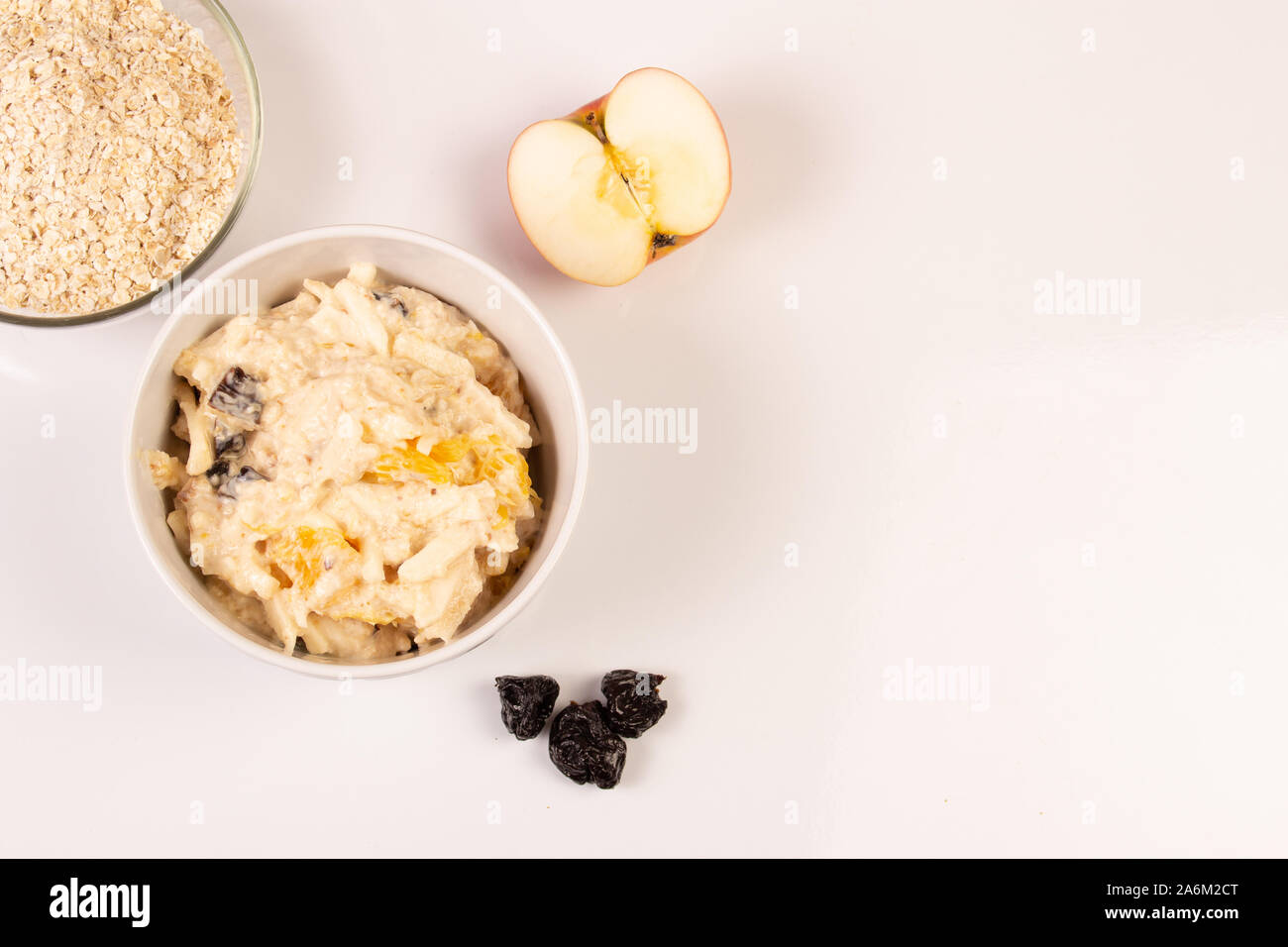 Salade de pomme, orange, avoine houblon et les pruneaux avec du miel dans une assiette blanche sur fond blanc. Banque D'Images