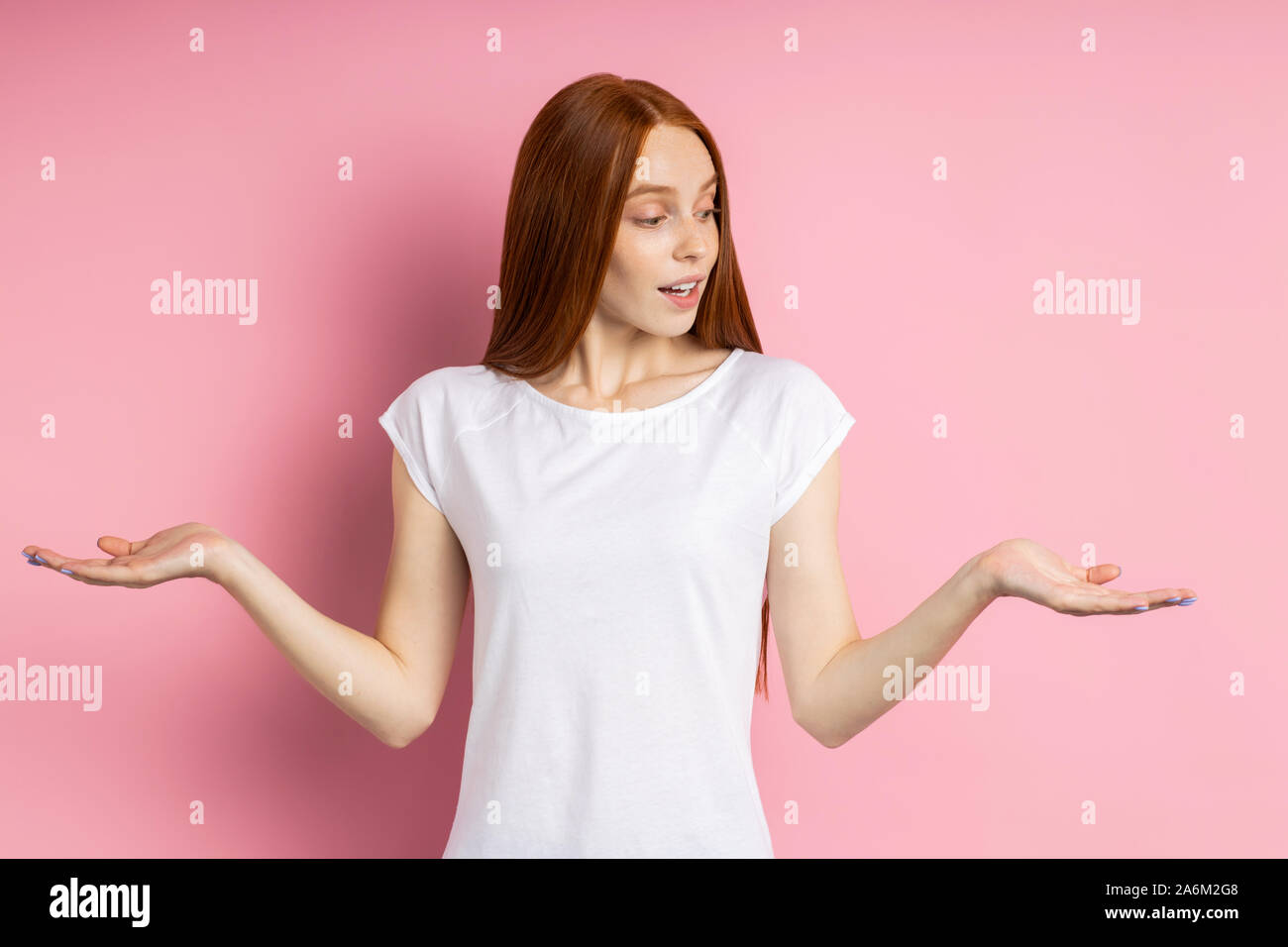 Heureux surpris charmant caucasian woman with red hair élever les deux paumes, holding copy space, démontrant deux articles, portant des vêtements décontractés ov isolés Banque D'Images