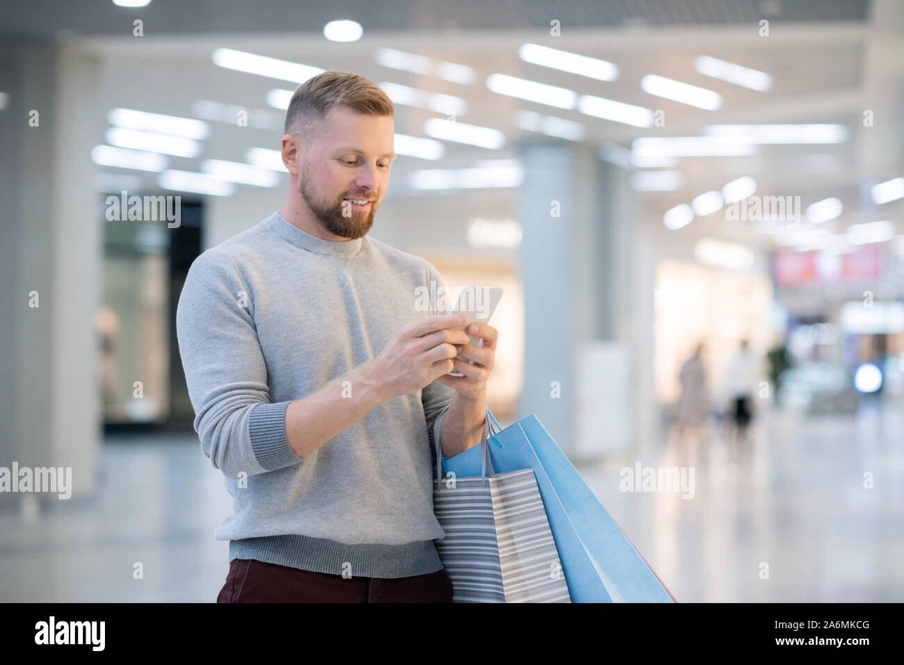 Jeune homme avec paperbags et smartphone à la promo à sur l'écran Banque D'Images