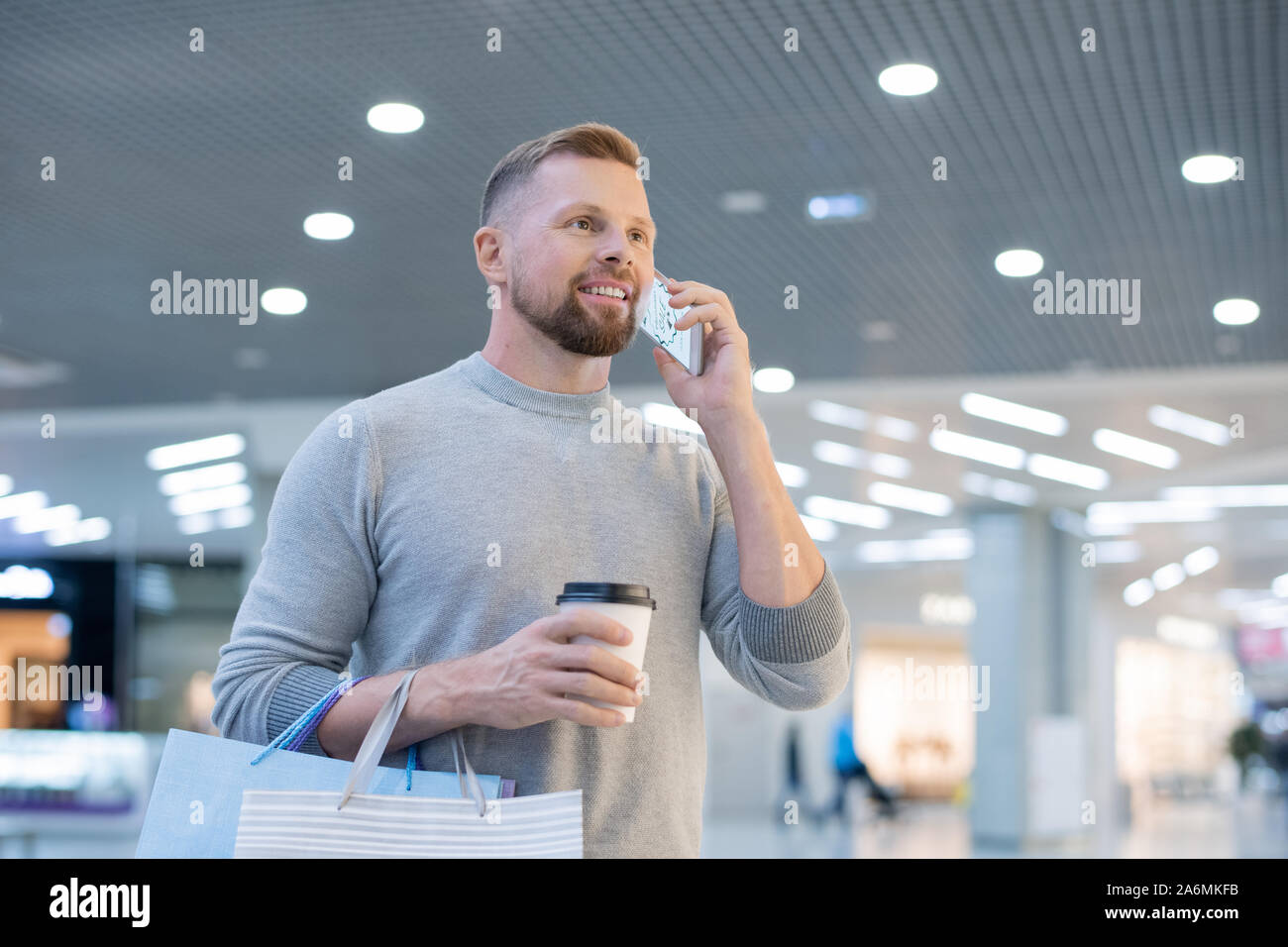 Jeune homme avec le smartphone, boire et paperbags appelant boutique en ligne Banque D'Images