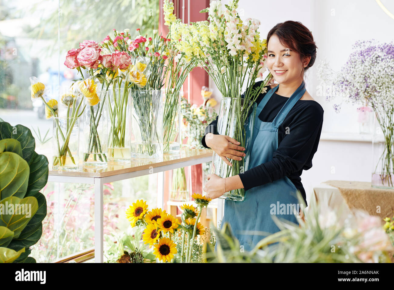 Smiling Young Asian woman plaçant des vases avec diverses belles fleurs en fleurs boutique Banque D'Images