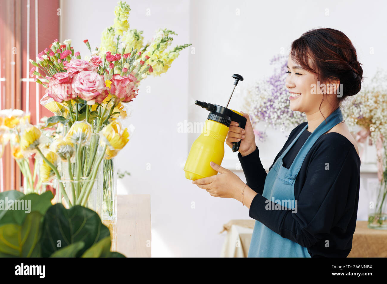 Cheerful young flower shop spaying travailleur et fleurs fraîches dans un vase de verre Banque D'Images