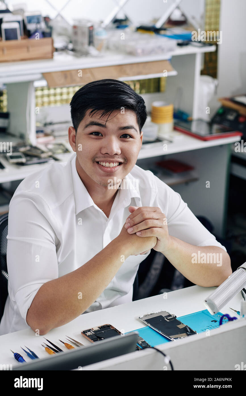 Cheerful handsome young man sitting at desk with smartphone démonté Banque D'Images
