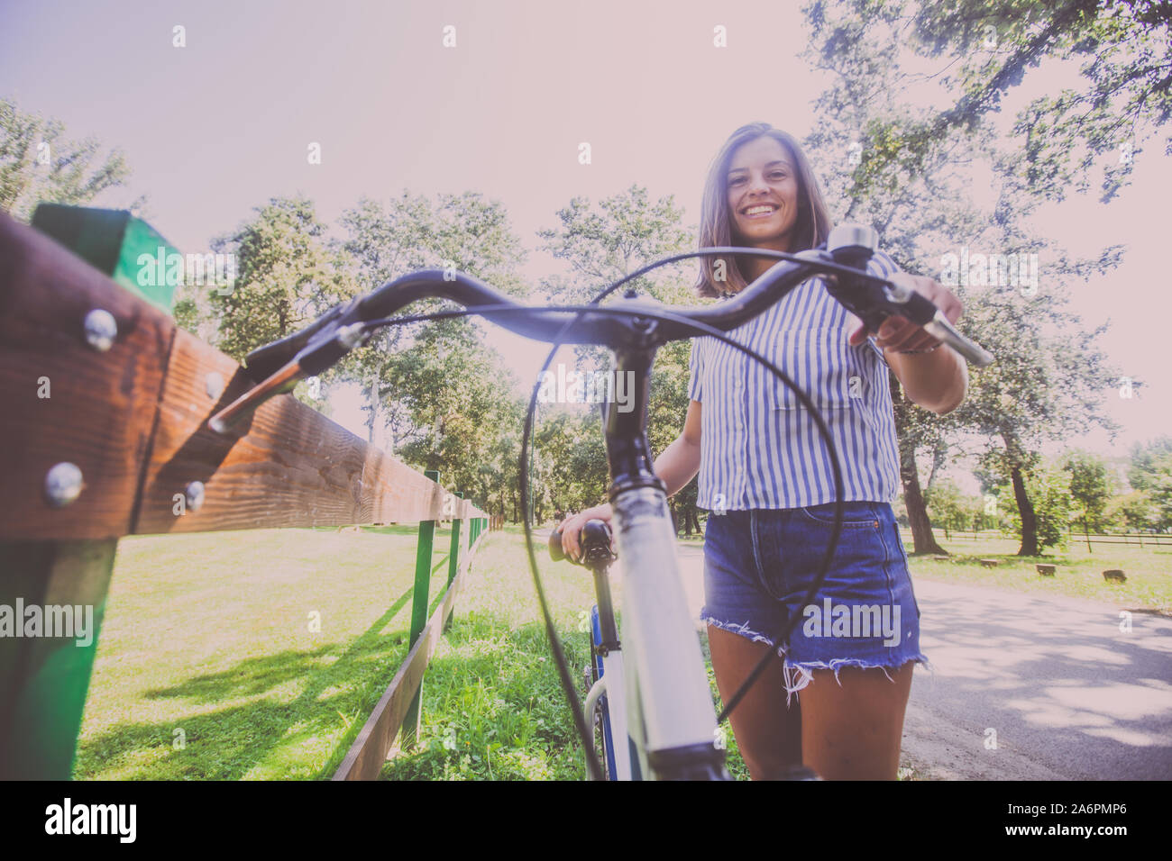 Portrait of attractive young woman in shorts jeans avec vélo dans le parc le jour d'été. Low angle view. Banque D'Images