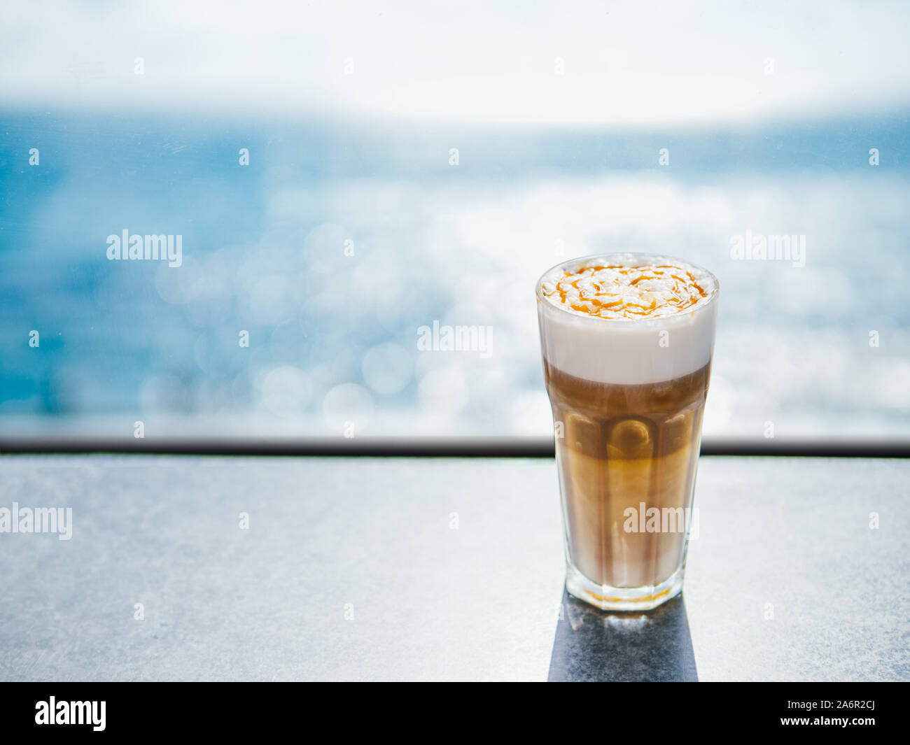 Sex latte macchiato caramel avec du café sur la table d'examen avec la mer bleu sur l'arrière-plan. La lumière du jour naturelle dure. Copier l'emplacement pour un texte ou un dessin Banque D'Images