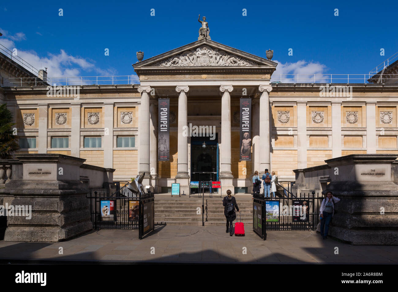 Une fille avec un cas à roues rouge vif se dirige vers les étapes à l'entrée de l'Ashmolean Museum, Oxford sur la rue Beaumont en plein soleil u Banque D'Images