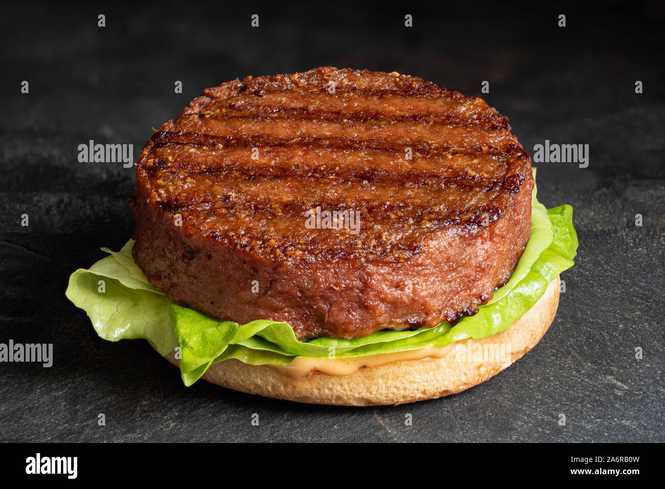 Base de plantes fraichement grillés sur patty burger bun avec laitue et de la sauce isolé sur l'ardoise noire. Banque D'Images