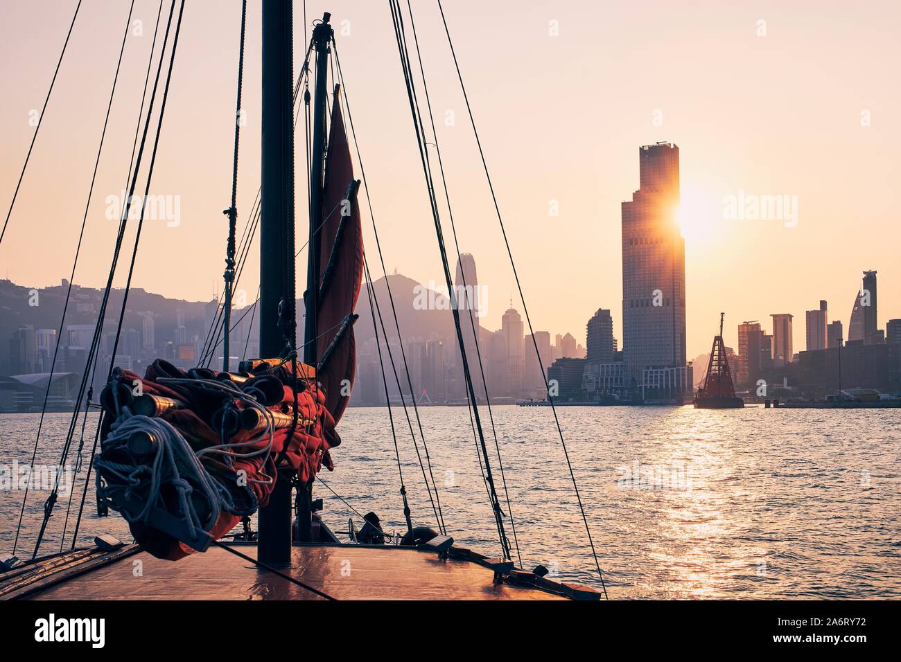Traversée en bateau jonque traditionnelle contre Victoria Harbour Hong Kong cityscape avec gratte-ciel au coucher du soleil doré. Banque D'Images