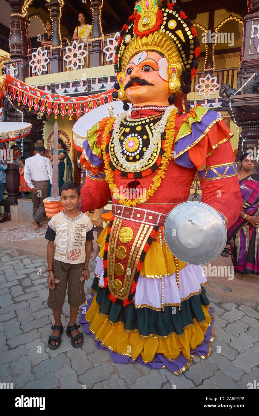 Au cours d'un festival autour du temple de Balkrishna à Udipi, Karnataka, en Inde, un garçon pose à côté de la figure de guerrier géant déplacé par un homme caché à l'intérieur Banque D'Images