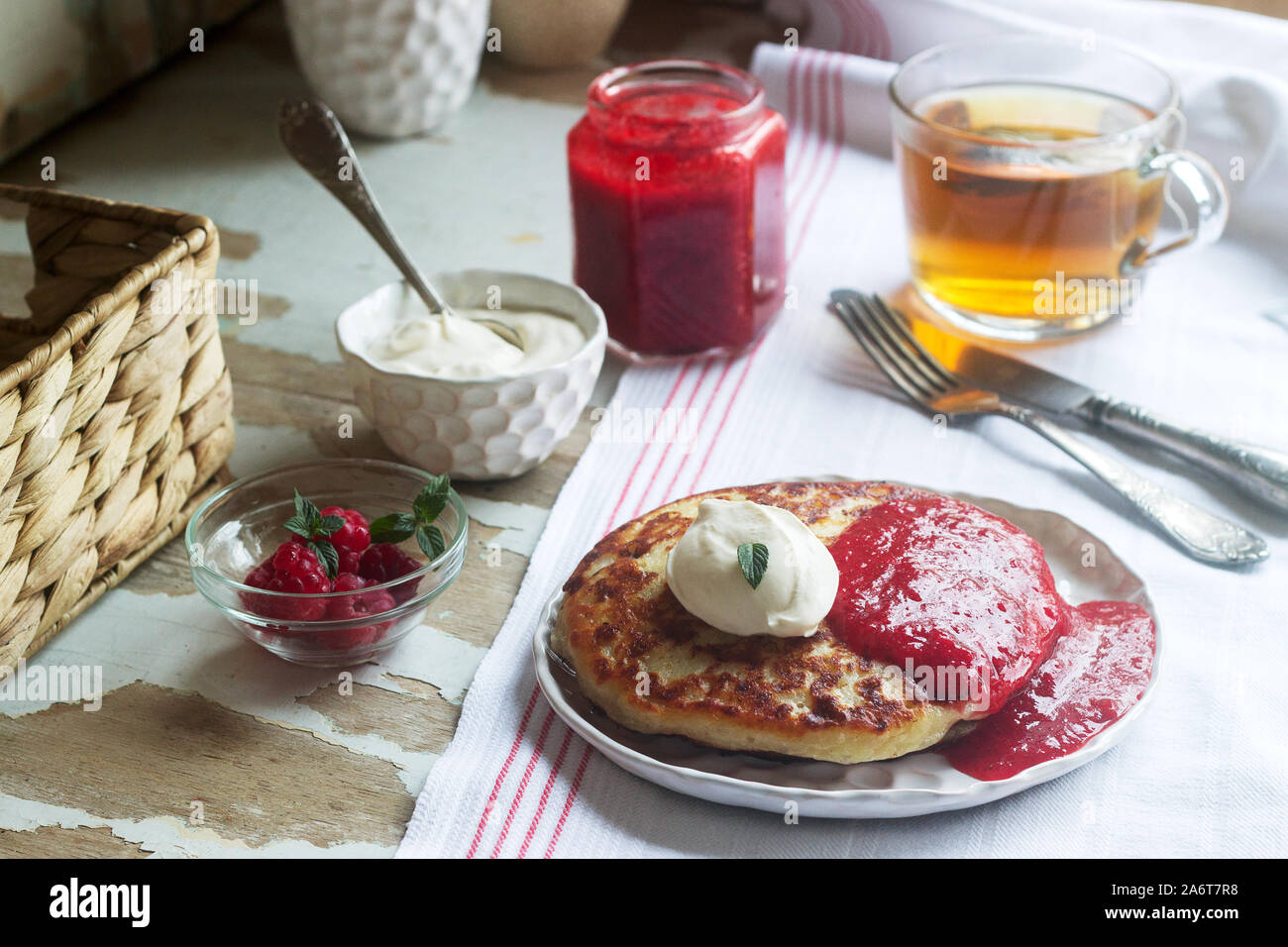 Crêpes caillé avec sauce aux fraises, crème aigre et framboises, et thé aux herbes sur une table légère. Style rustique. Banque D'Images