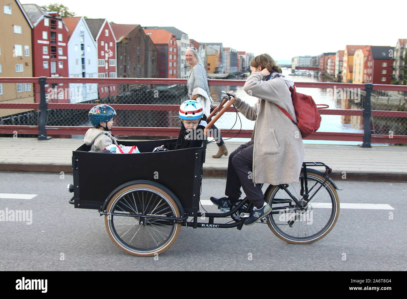 Femme sur tricycle porte deux enfants. Banque D'Images