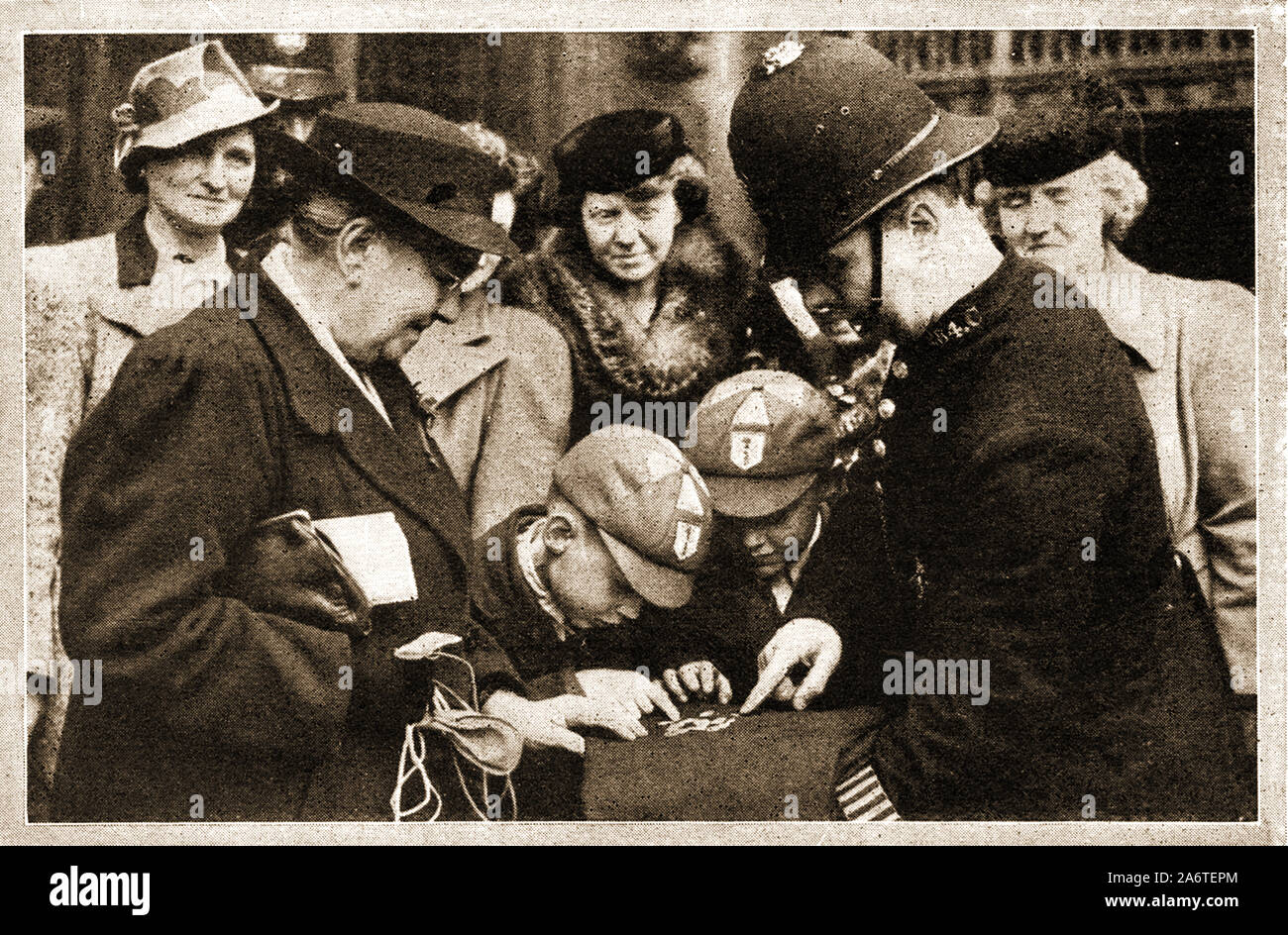 MAUNDAY / ARGENT SAINT Circa 1940 - Les enfants d'examiner les pièces d'argent distribué par le roi George VI d'Angleterre après la la cérémonie annuelle de la distribution d'argent dans l'église Saint d'Angleterre service religieux qui a eu lieu le Jeudi Saint, le jour avant le vendredi saint, lorsque le monarque britannique solennellement distribue des petites pièces d'argent connue sous le nom de 'Maundy argent' comme une aumône symbolique. Un 'Bobby' affiche sur son manteau. Banque D'Images