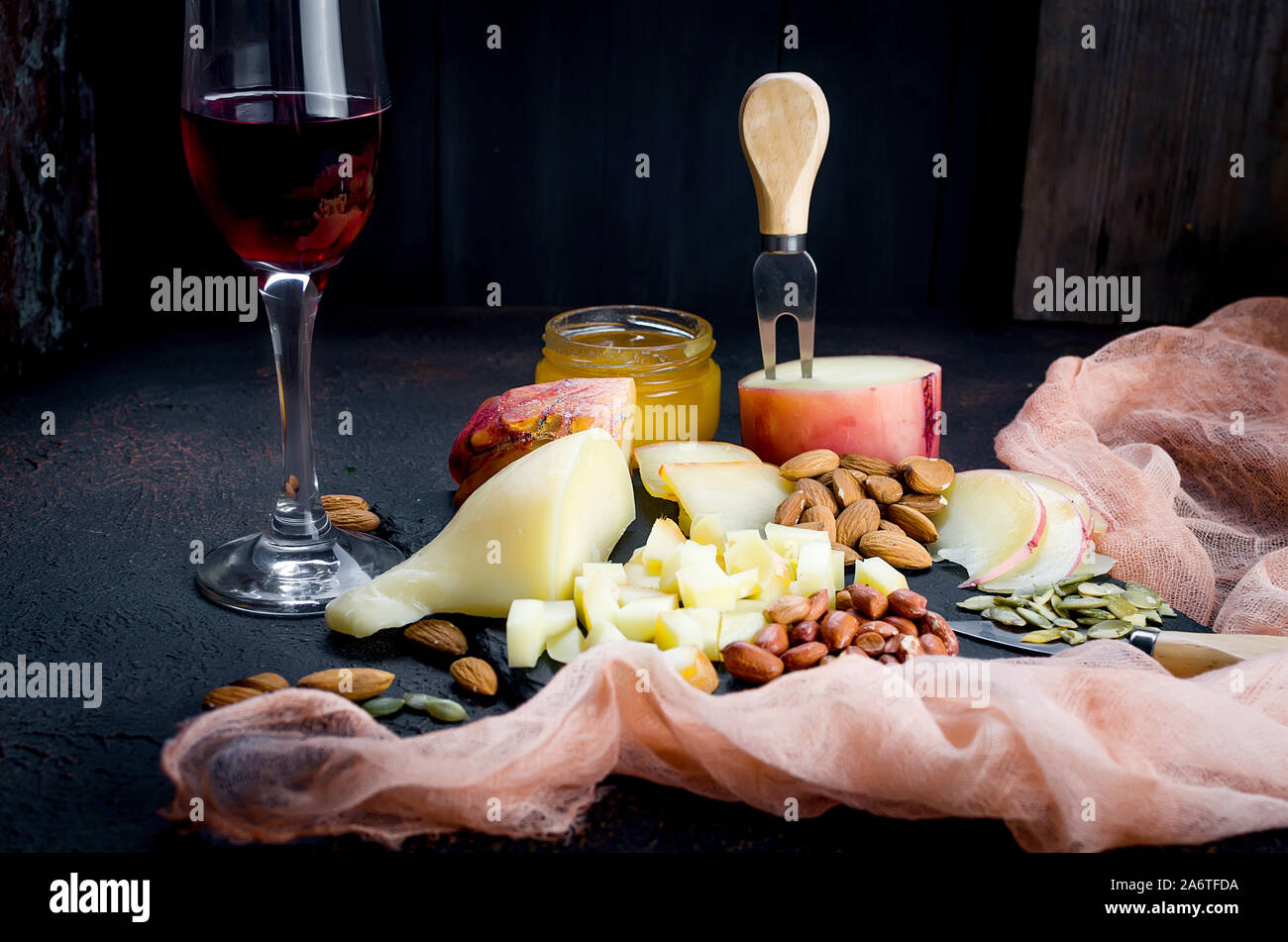 Verre de vin rouge, différentes variétés de fromage, d'amandes, miel en pot sur table en bois foncé Banque D'Images