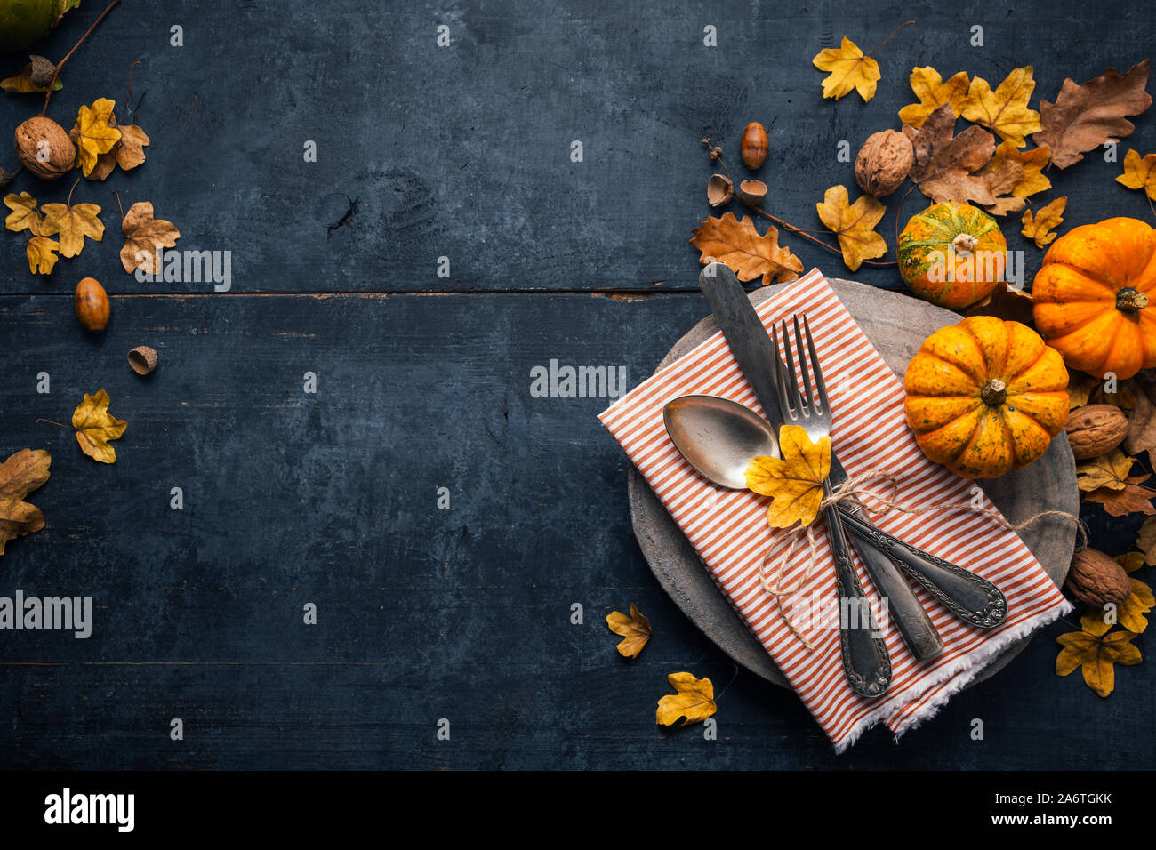Arrière-plan de l'action de grâce, avec des couverts sur une plaque de bois, de petites citrouilles et feuilles sèches sur une table en bois bleu. Vue d'en haut Banque D'Images