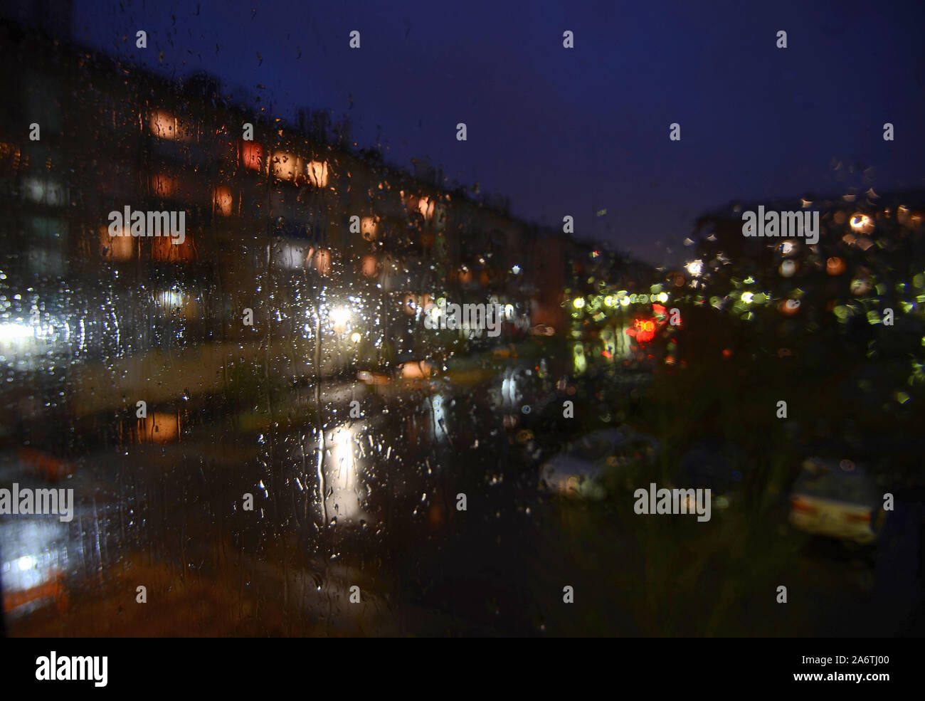 Sityscape pluvieux nuit à l'extérieur de la fenêtre - volet arrière-plan flou flou artistique avec des gouttes d'eau sur le verre, de l'éclairage de nuit, flou des voitures en stationnement. Mela Banque D'Images