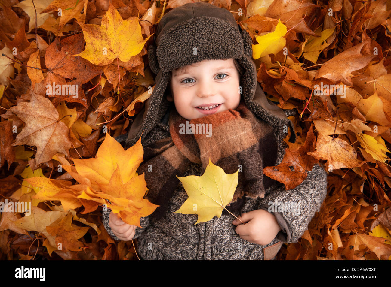 Cute little Woman est tombé en portant de belles feuilles aux couleurs automnales smiling portant un foulard et d'un cavalier en tricot vintage aviator hat Banque D'Images