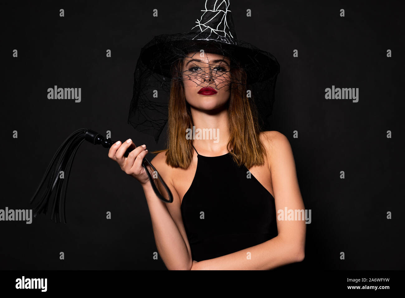 Jolie femme au chapeau de sorcière tenant le fouet fouet isolated on black Banque D'Images