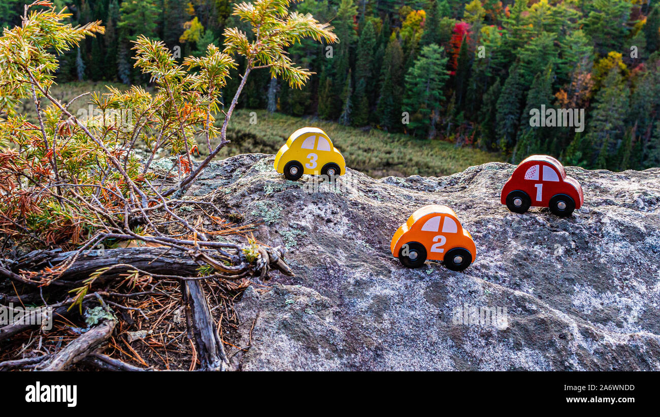 Une série de rouge, orange et jaune toy cars, numérotées 1, 2 et 3, s'asseoir sur la pierre d'une falaise surplombant une forêt. Les jouets en bois sont placées à côté de Banque D'Images