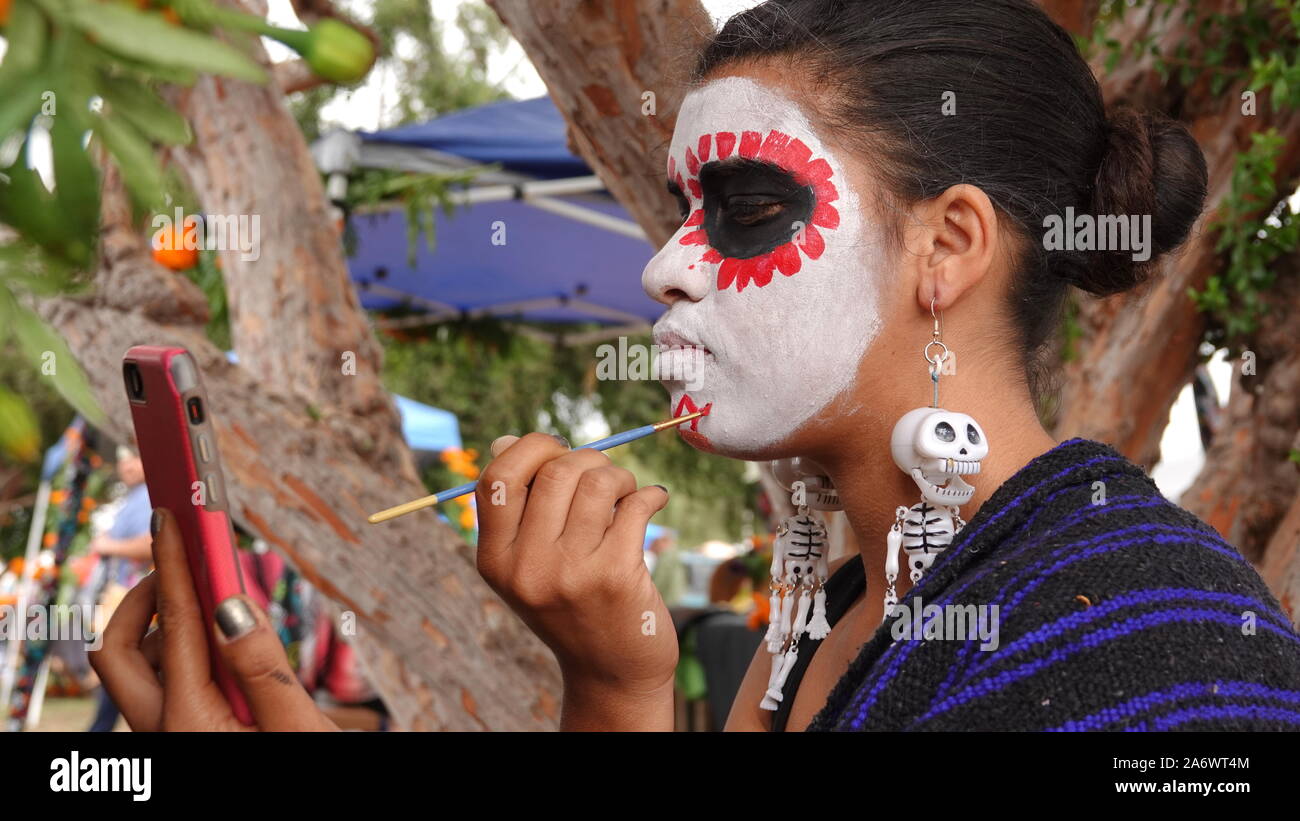 Une jeune femme hispanique sur crâne en sucre à l'aide de maquillage son téléphone appareil photo comme un miroir. Banque D'Images