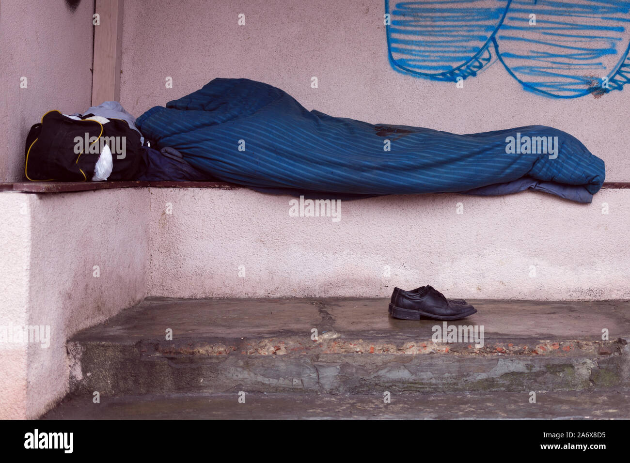 Sans-abri dormir sur la station de bus. Ses chaussures couché à côté de lui. Banque D'Images